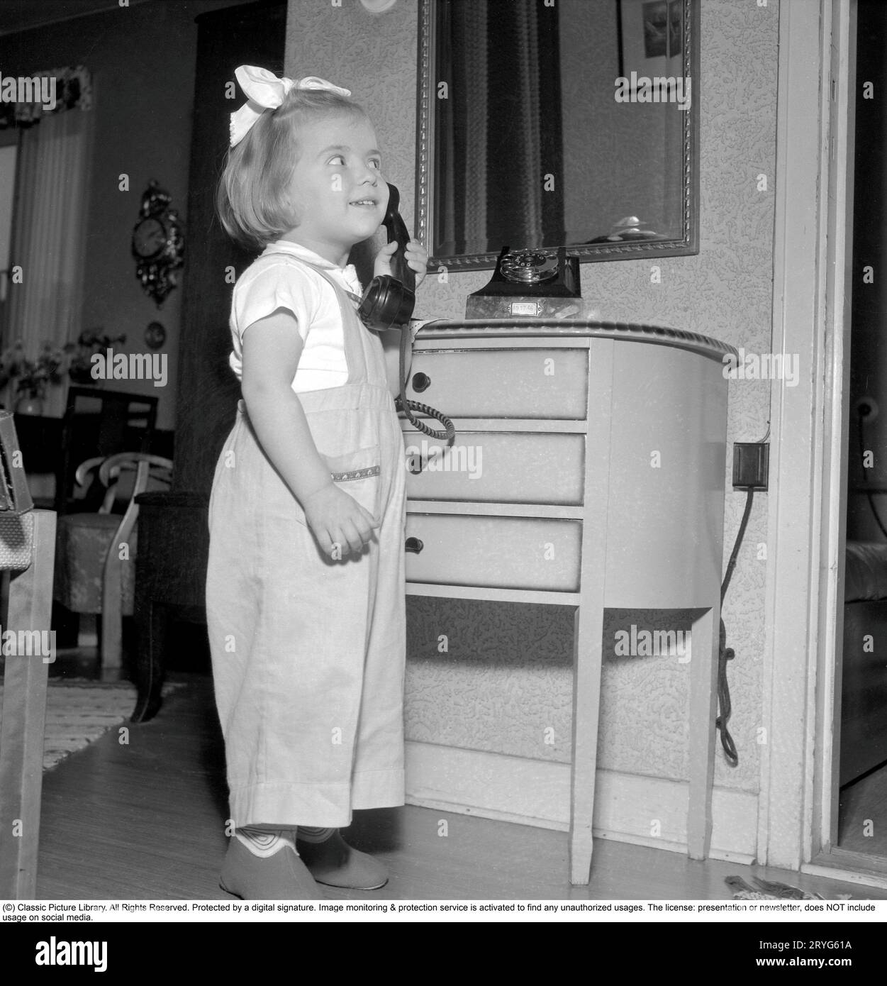 In the 1950s. A little girl is playing with a telephone, holding the handset, reciever against her ear to listen. Sweden 1950. Conard ref 1526 Stock Photo