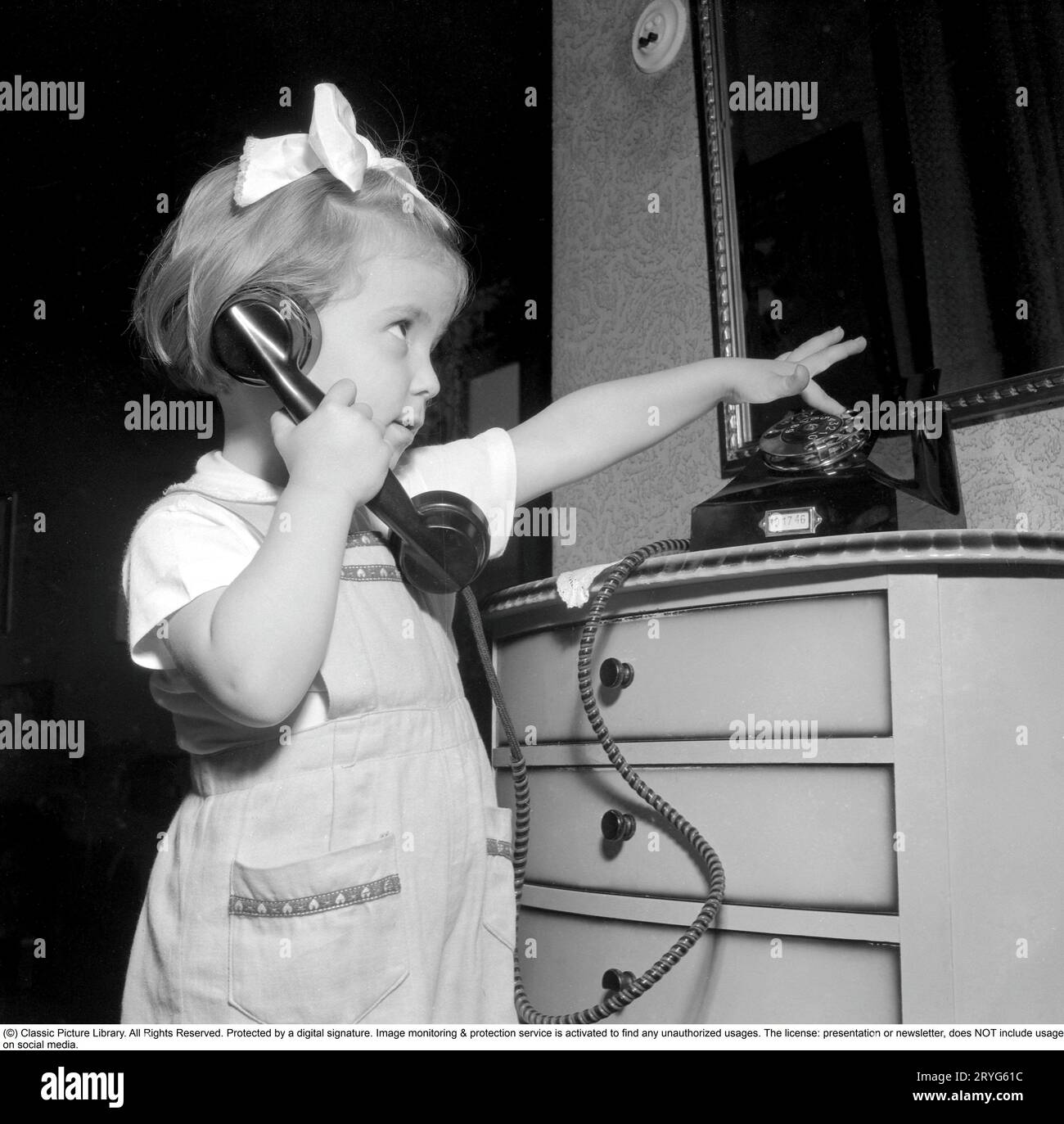 In the 1950s. A little girl is playing with a telephone, holding the handset, reciever against her ear to listen. Sweden 1950. Conard ref 1526 Stock Photo