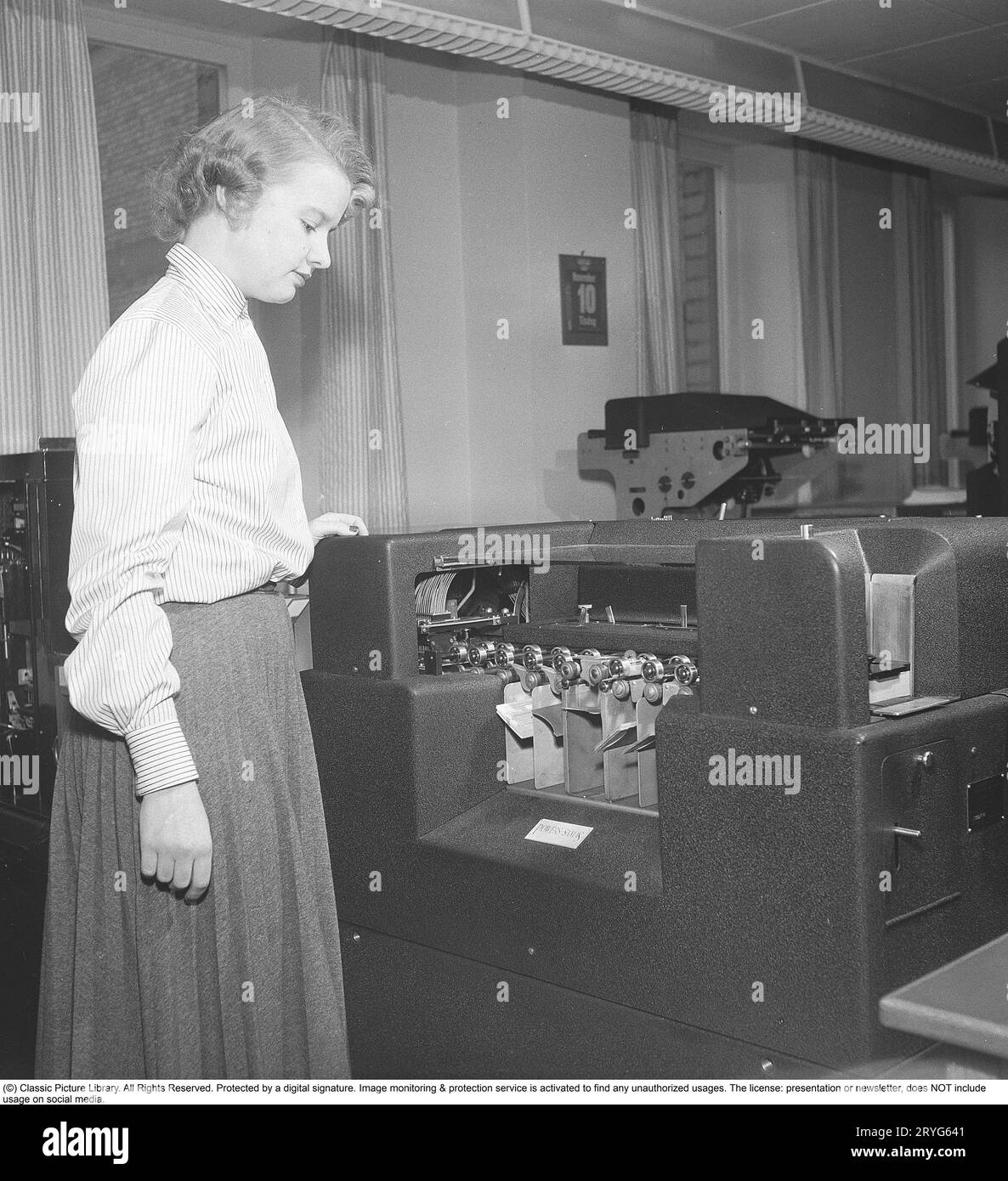In the 1950s. A female clerk at punch card reader machine overlooking it's function and the feed of  the punch cards into the machine. Punched cards was created by another machine, entering information, creating the punch cards as a storage medium where the punched holes in the paper card were the input information. The picture shows the reader sorting the cards after having read the information in the punch holes. The machine is made by the british manufacturer Powers-Samas who developed the encryption machine, far better and safer then the german Enigma.  Sweden 1954. Kristoffersson ref BM85 Stock Photo