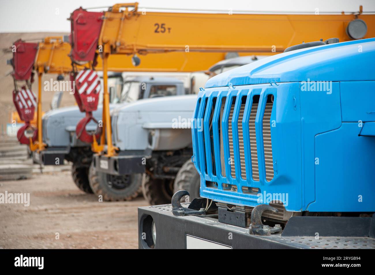 A closeup row of large truck cranes and machines at an industrial construction site Stock Photo