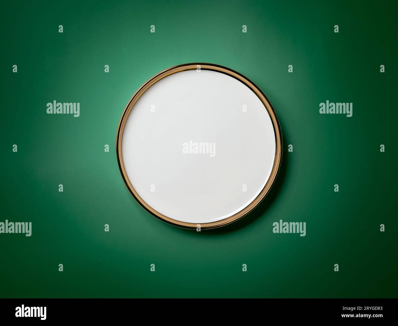 Empty white round plate with golden border on deep green background Stock Photo