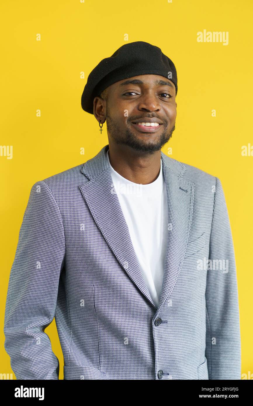 Happy handsome smiling to camera on yellow background. Young man in grey suit wearing black beret. Youth concept. Stock Photo