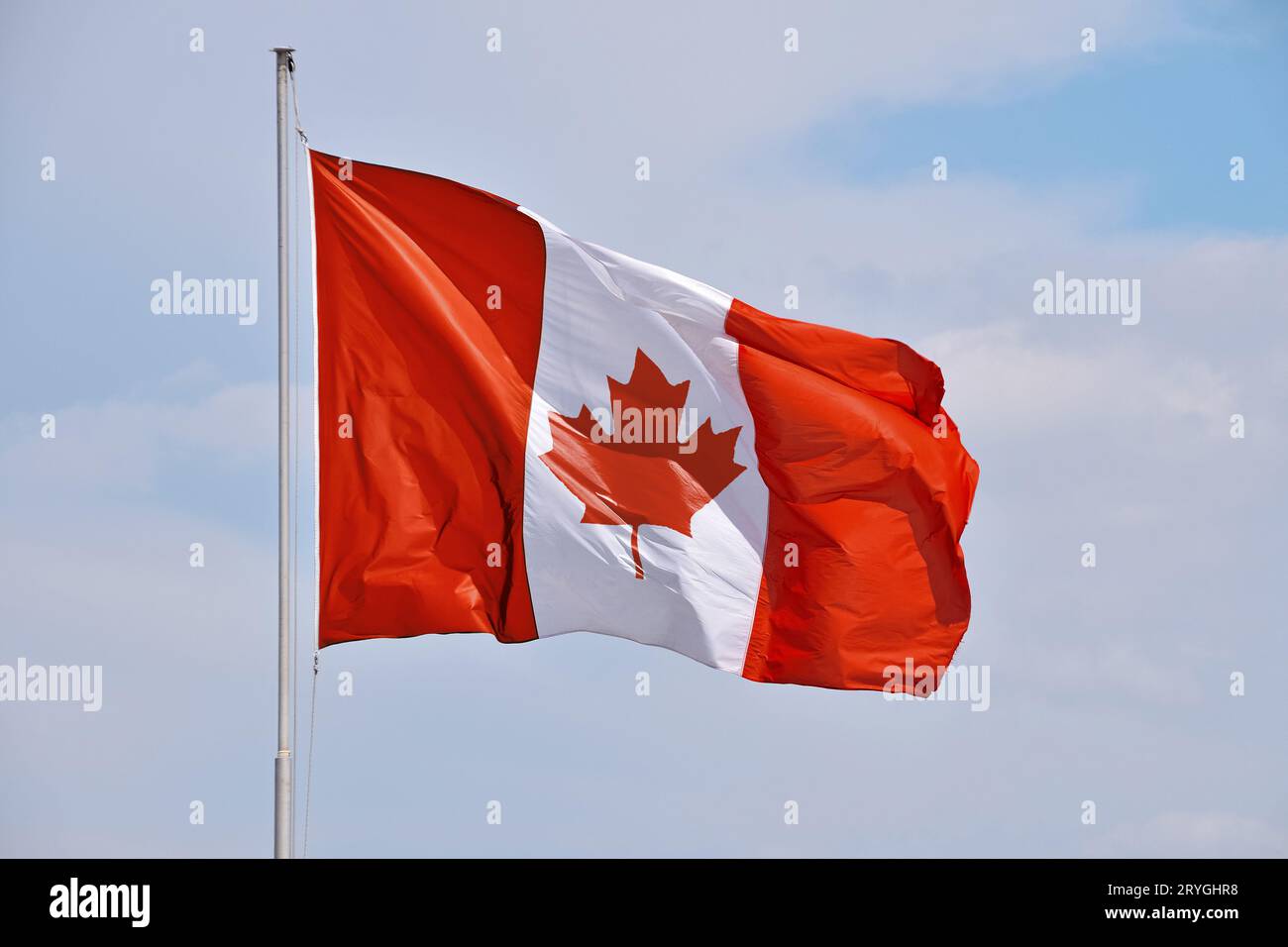Canadian flag waving in cloudy blue sky Stock Photo