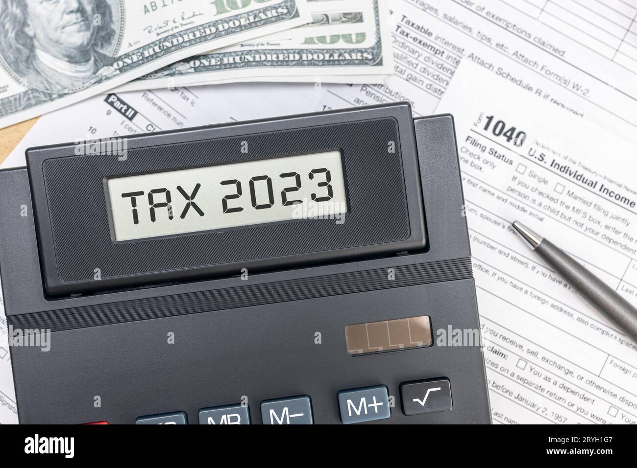 Tax time 2023 concept. Text on calculator screen, tex forms and dollar banknotes on table. Top view Stock Photo