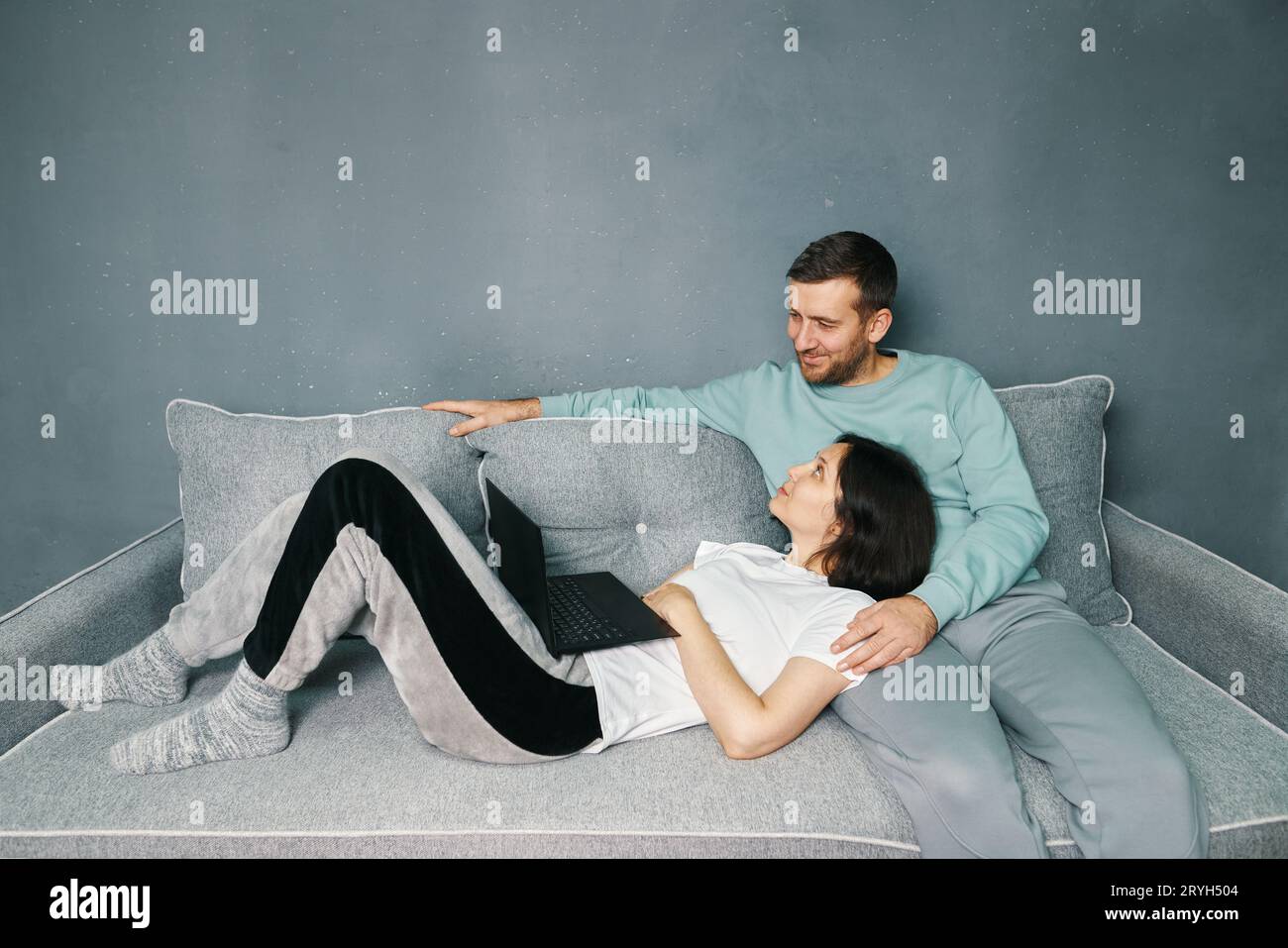 Happy couple embracing using laptop together relaxing on sofa at home Stock Photo
