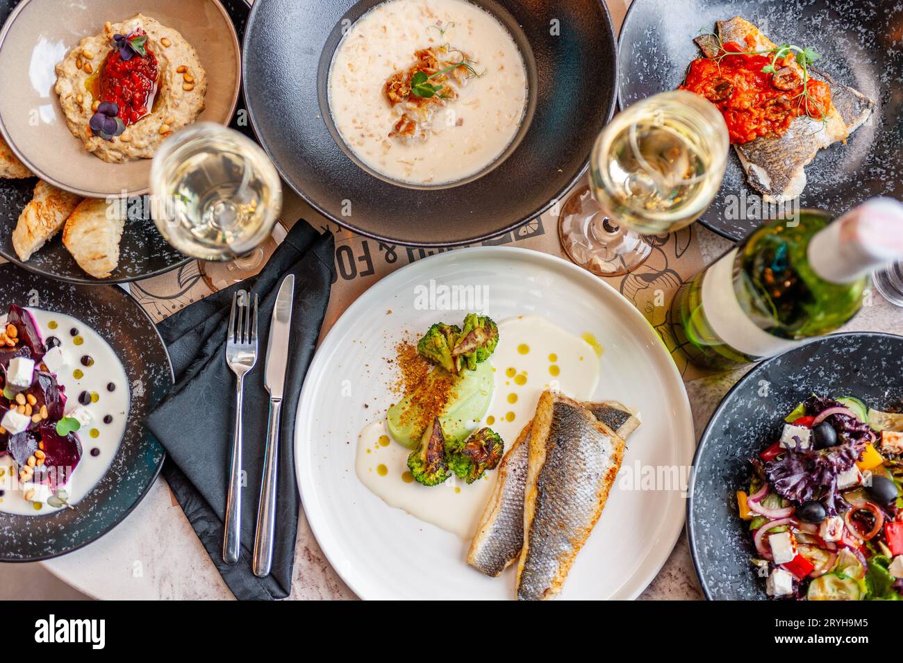 A set of Mediterranean cuisine dishes on a table in a restaurant with a glass and a bottle of white wine. View from above. High quality photo Stock Photo