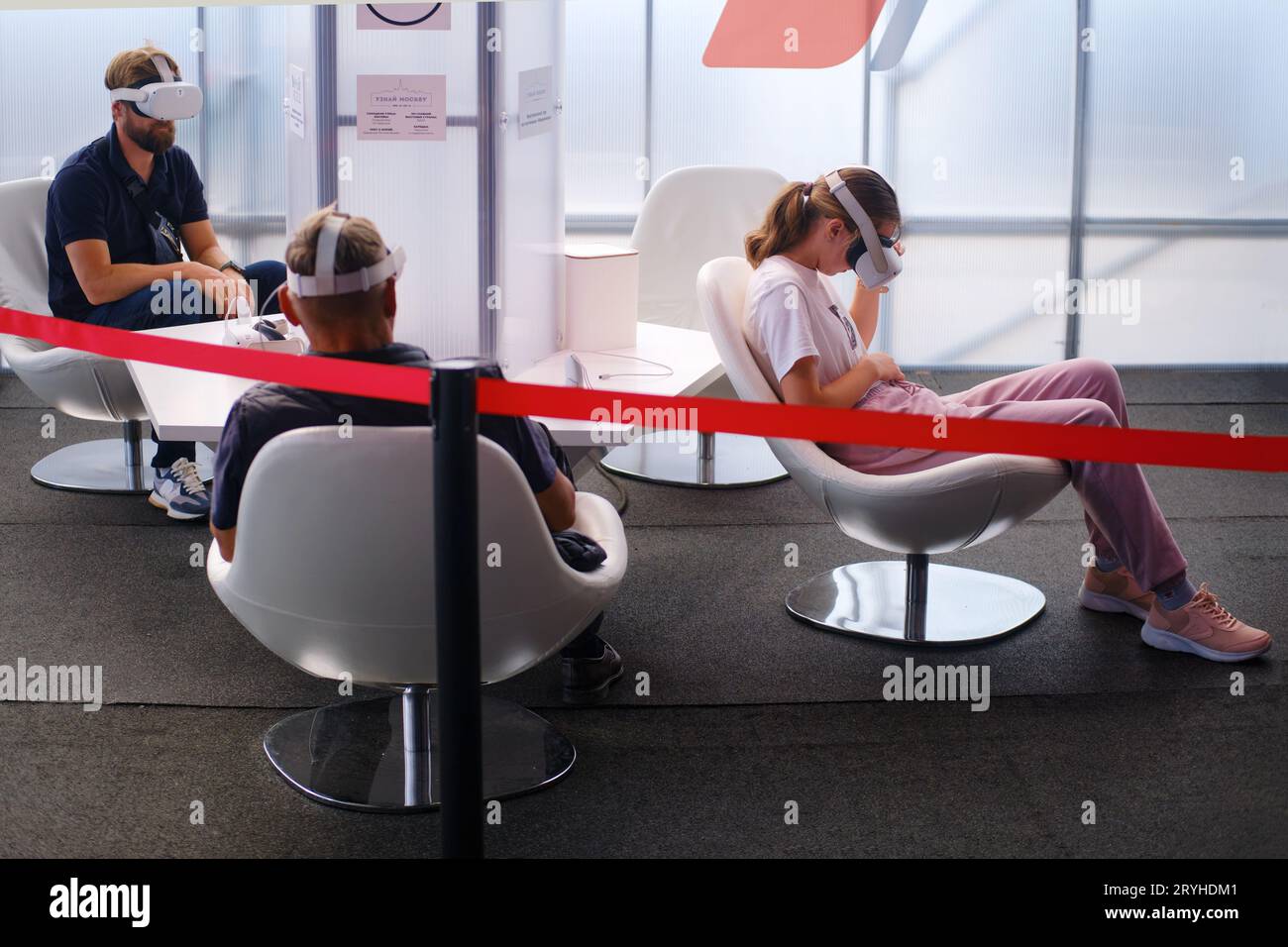 Young woman using virtual reality headset while sitting in waiting room - Moscow, Russia, 05 September 2023 Stock Photo