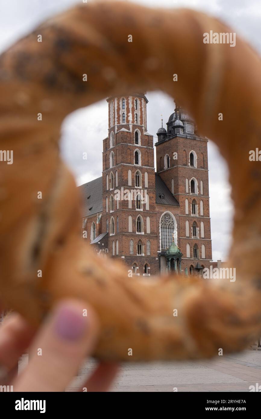 Tourist woman eating bagel obwarzanek traditional polish cuisine snack waling on Market square St. Mary's Basilica on the Krakow Stock Photo