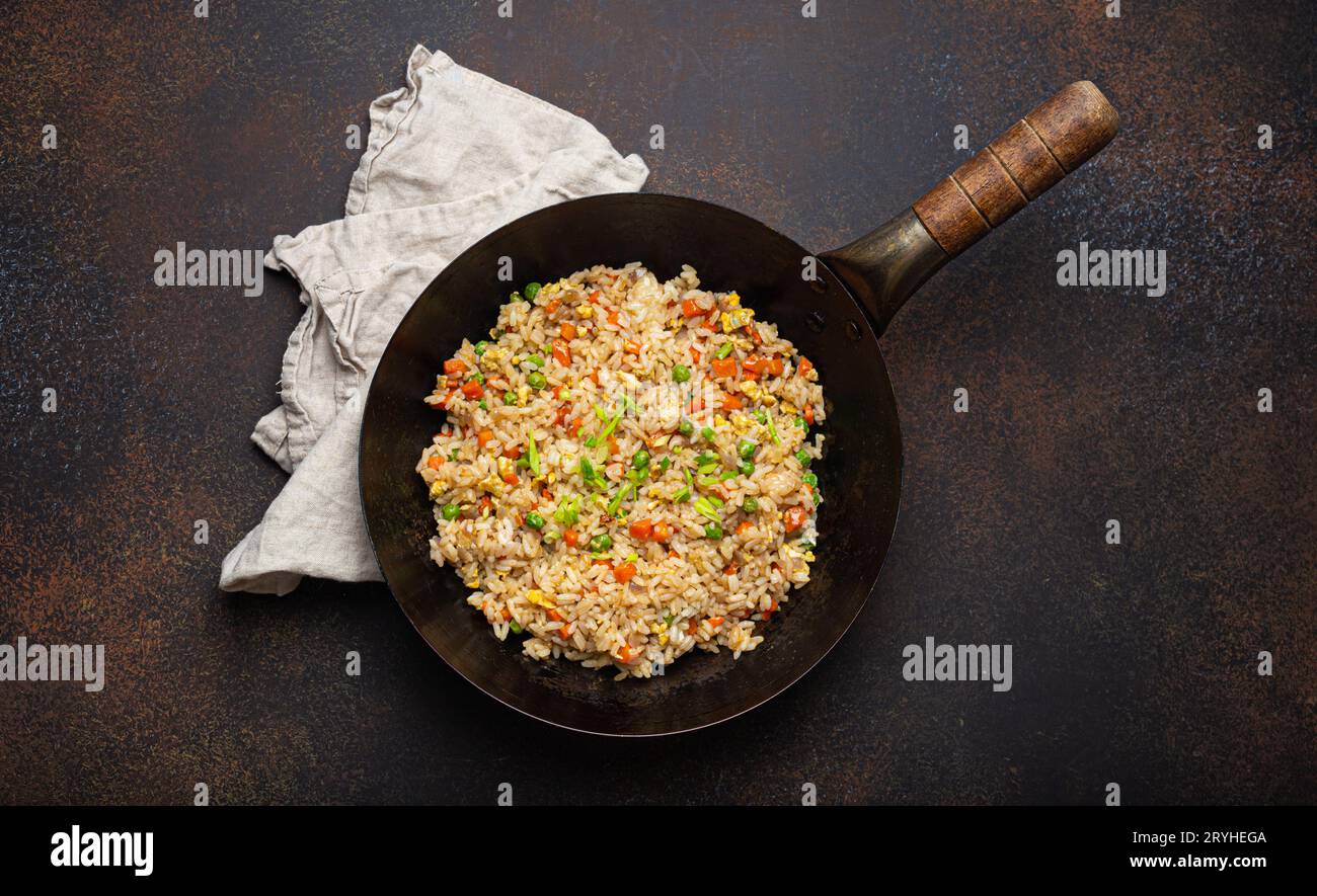 Authentic Chinese and Asian fried rice with egg and vegetables in wok top view, rustic concrete table background. Traditional di Stock Photo