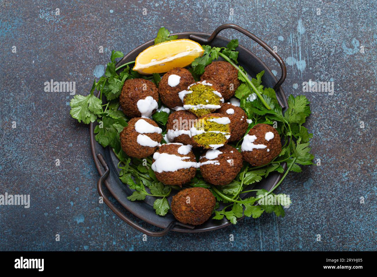 Plate of fried falafel balls served with fresh green cilantro and lemon, top view on rustic concrete background. Traditional veg Stock Photo