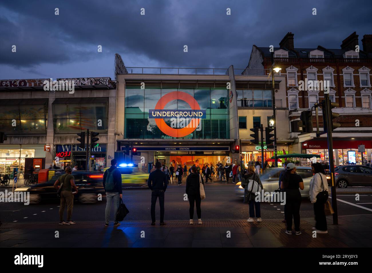 Brixton, London, UK: Pedestrian crossing on Brixton Road opposite Brixton underground station. Evening view with people, traffic and a police car. Stock Photo