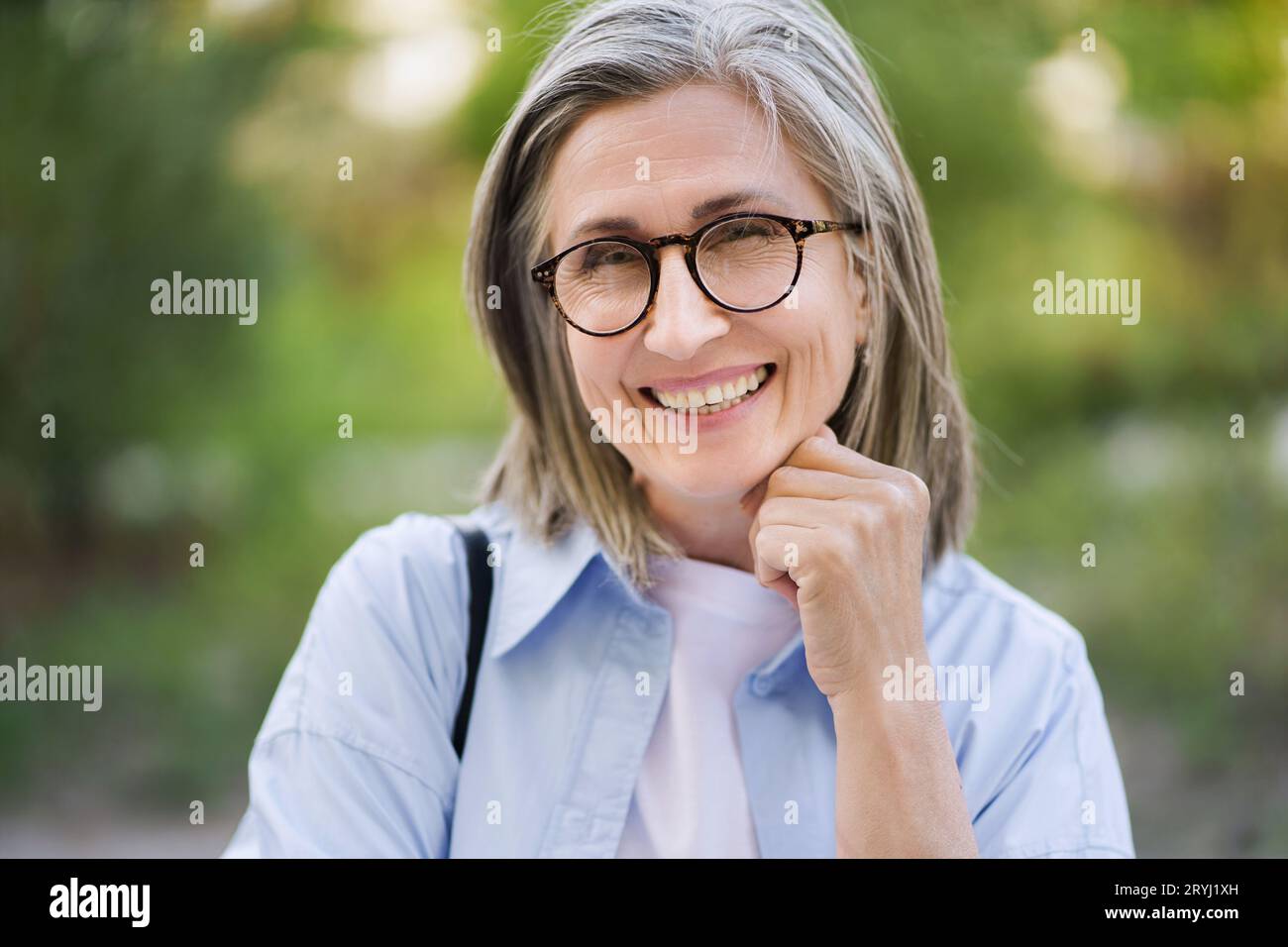 Happy mature woman with silver hair and glasses smiling outdoors, showcasing the beauty of aging and positive attitude towards l Stock Photo