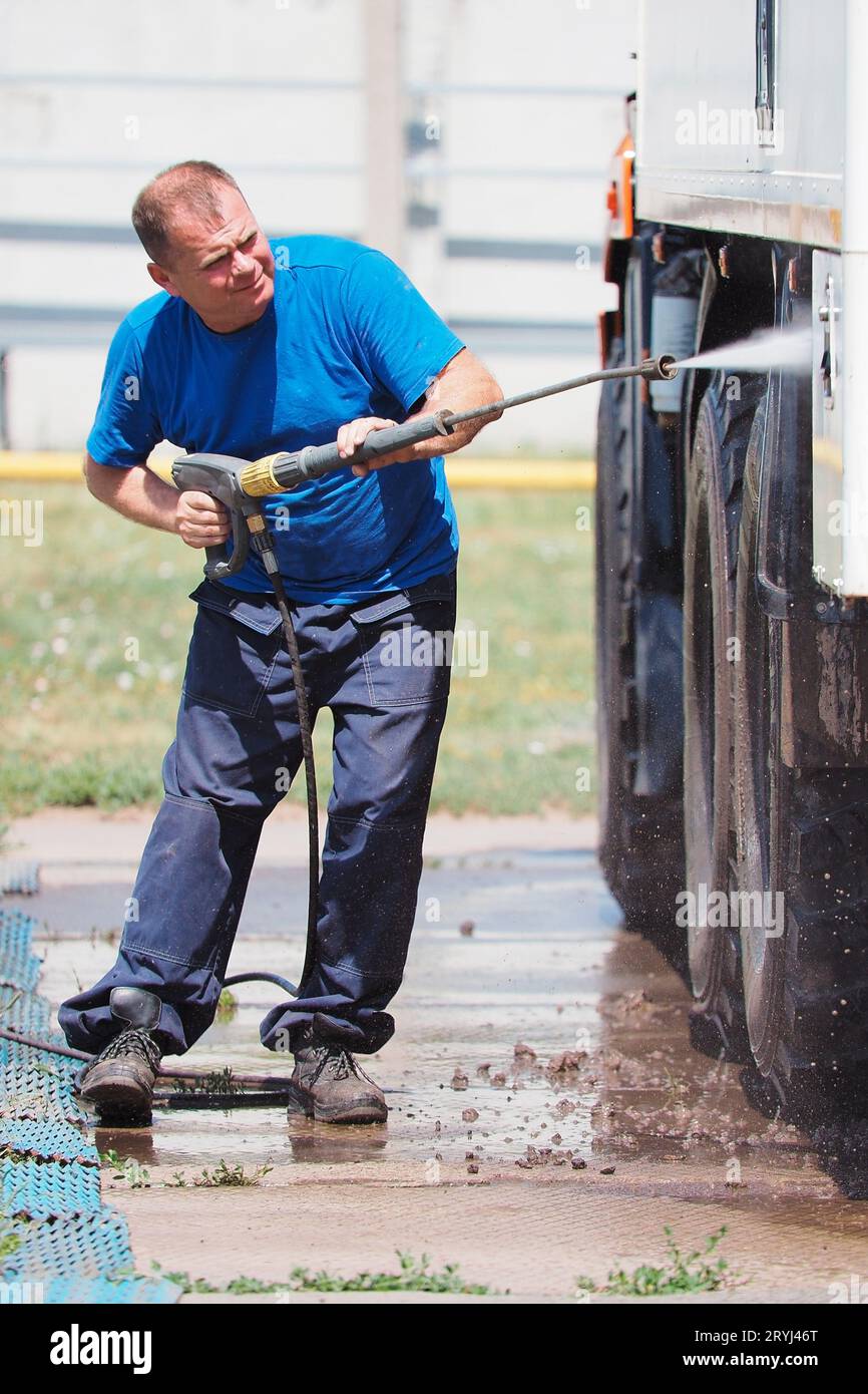 Car wash for heavy and cargo vehicles. Male car washer in washes a truck with a water gun on the street on a summer day. Stock Photo