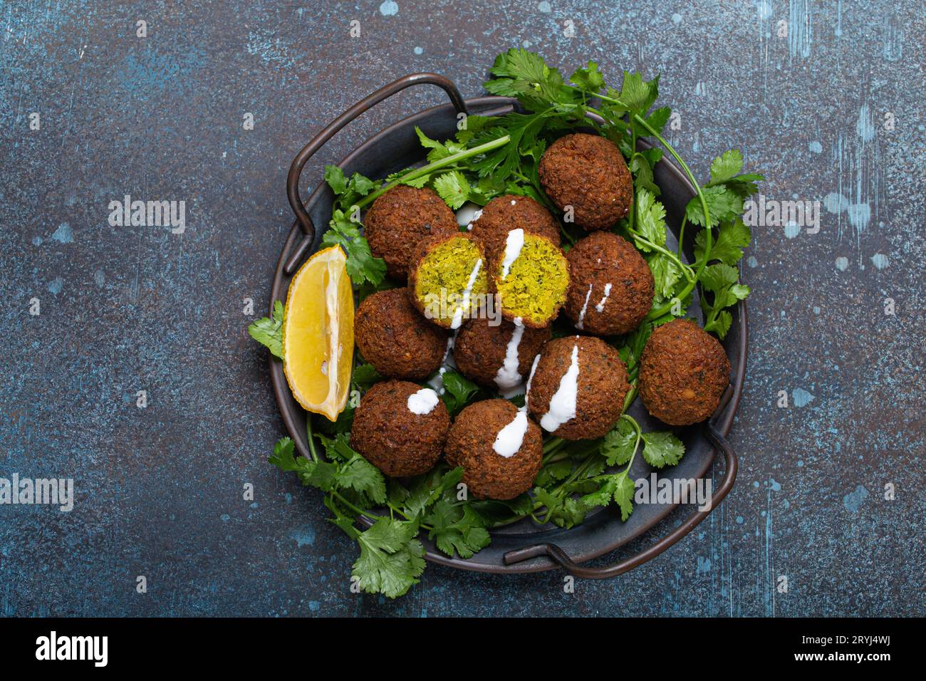 Plate of fried falafel balls served with fresh green cilantro and lemon, top view on rustic concrete background. Traditional veg Stock Photo