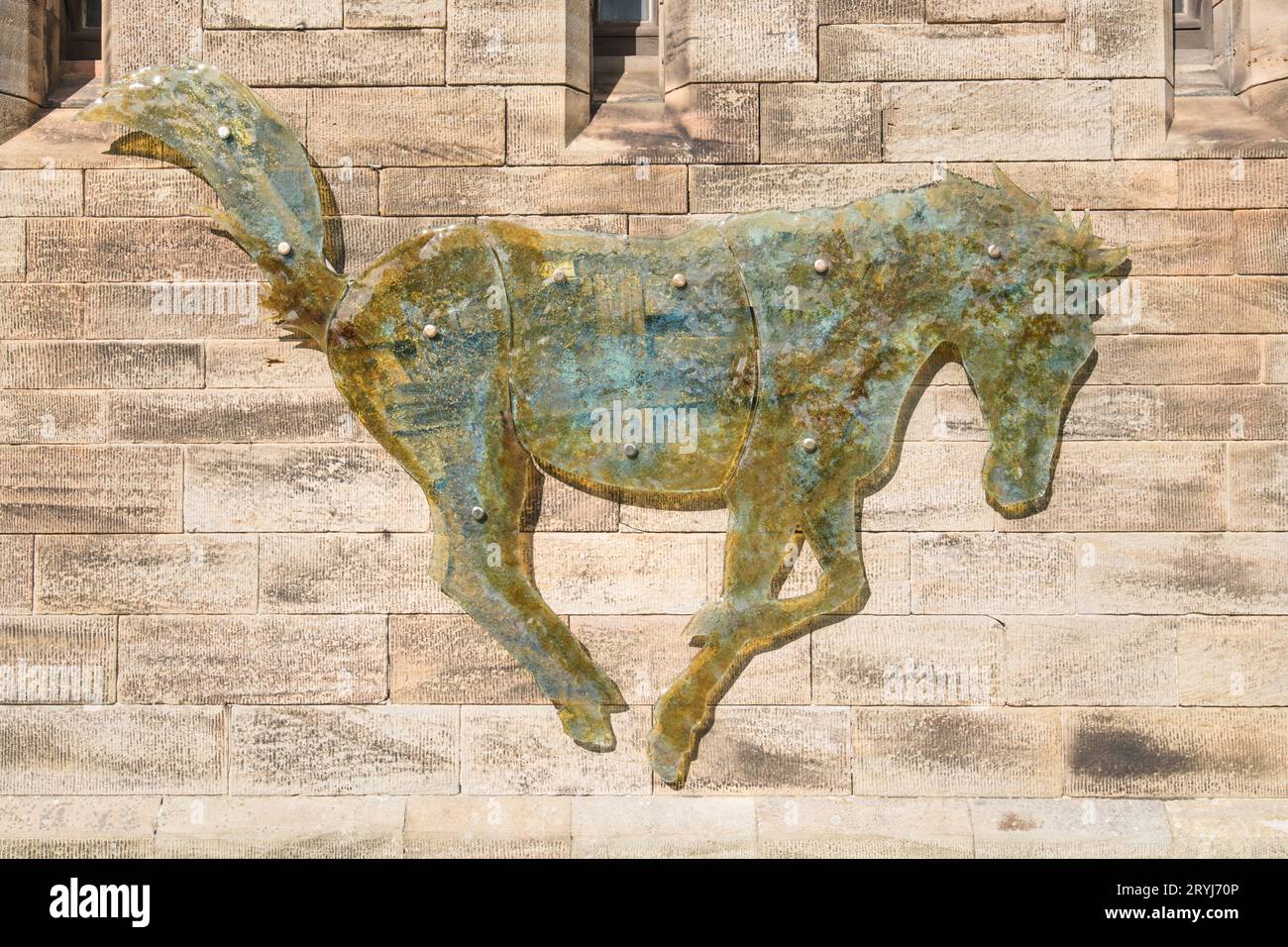 Full-size galloping glass horse, by  glass artist Rena Holford, on the outside of the stable wall at Bamburgh Castle. Stock Photo