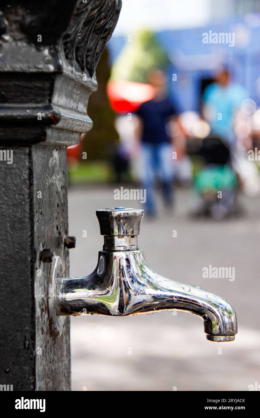 outdoor public water tap in central London with blurred out family wearing colourful clothing in the background July 2010 Stock Photo