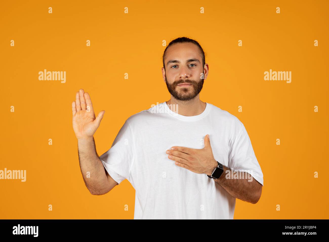 Serious confident adult european guy with beard puts hand to chest, making gesture I swear, take oath, promise Stock Photo