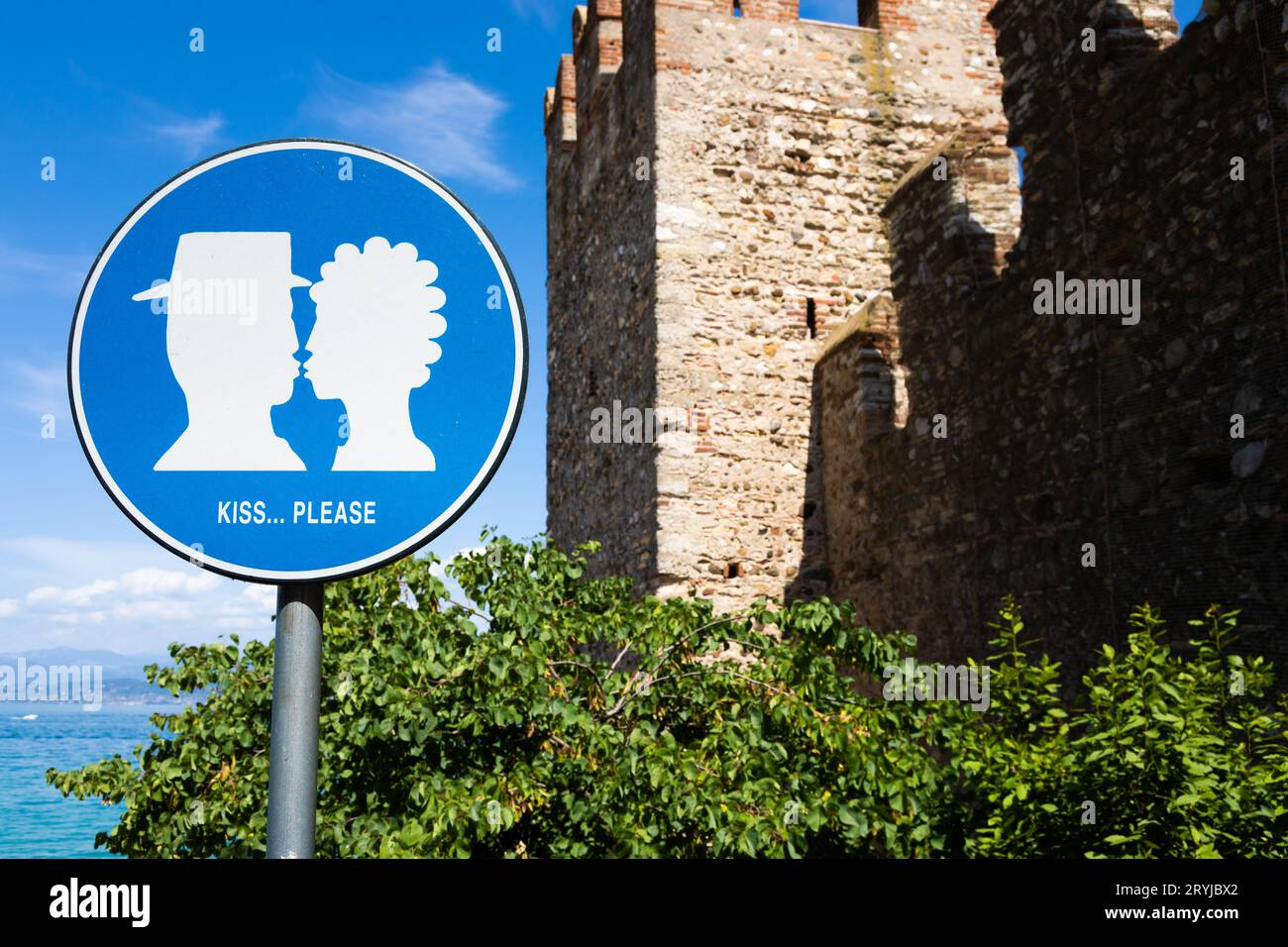 Kiss street sign located in public area in front of Sirmione castle, Italy. Concept of love, couple, romantic. Stock Photo