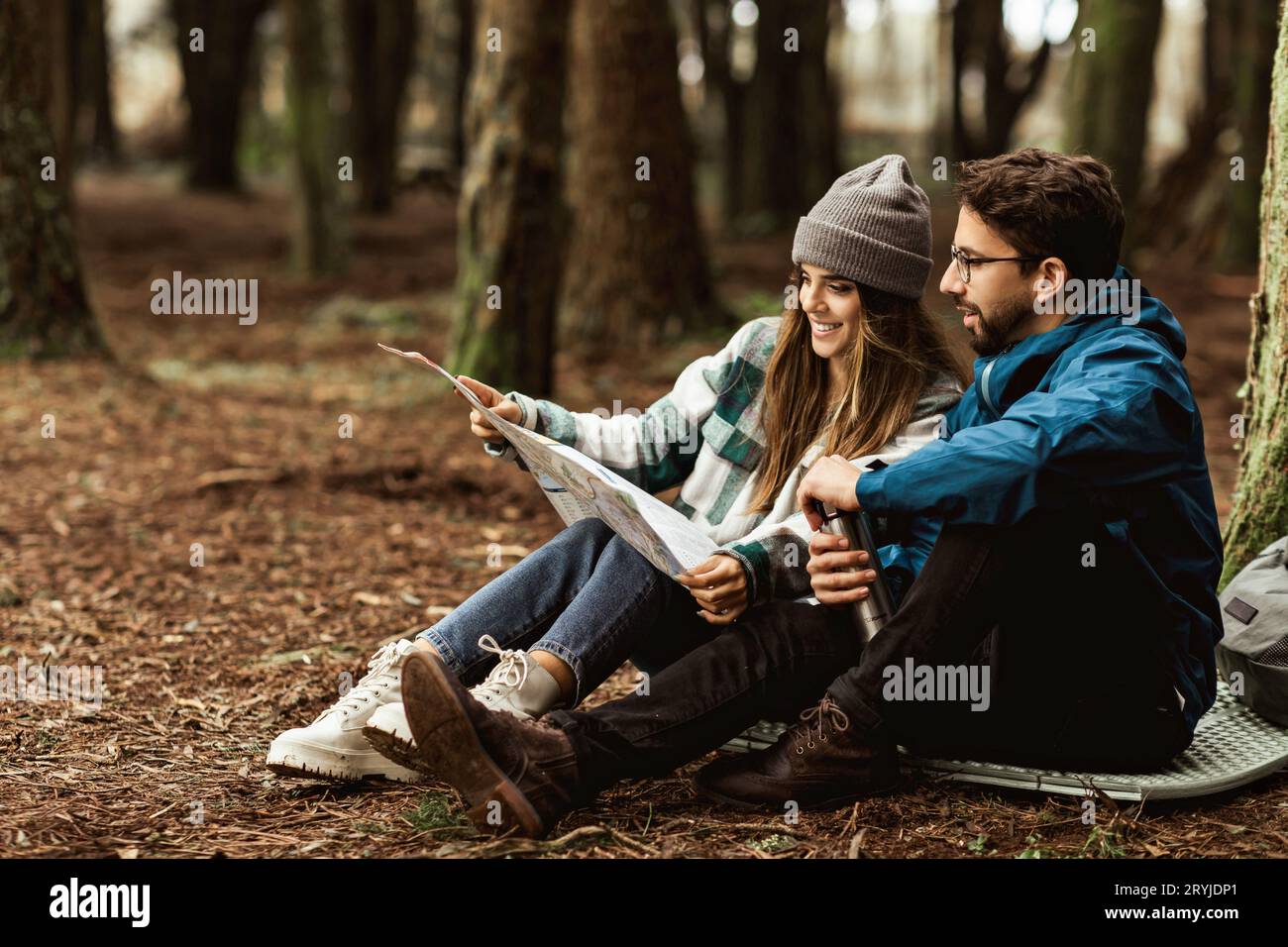 Happy young caucasian family in jackets relaxing, look at route map, enjoy adventure in cold forest in autumn Stock Photo