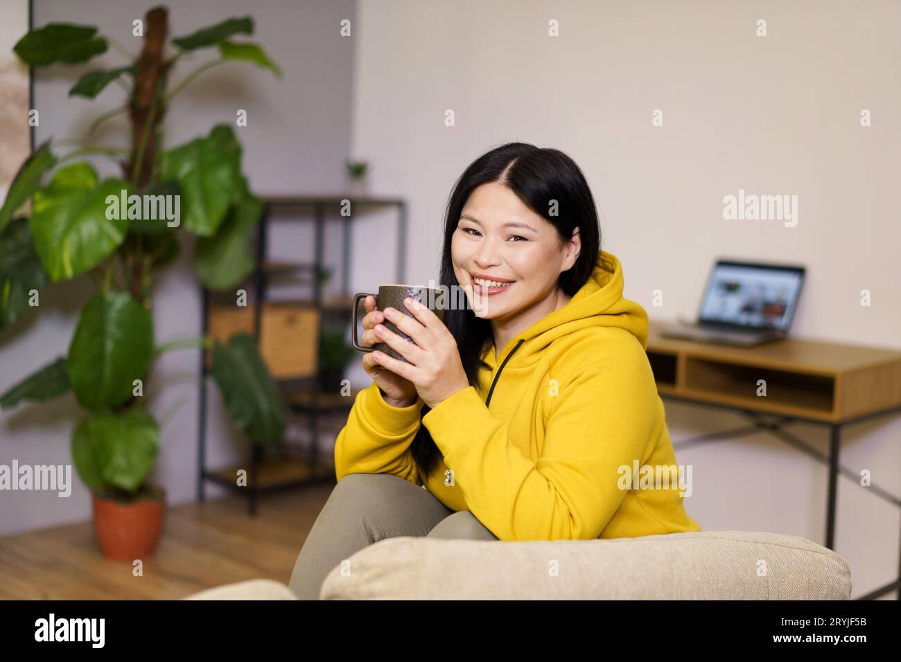 Cute Asian woman takes break from her online work at home to enjoy a soothing cup of tea. The image captures the balance of work Stock Photo