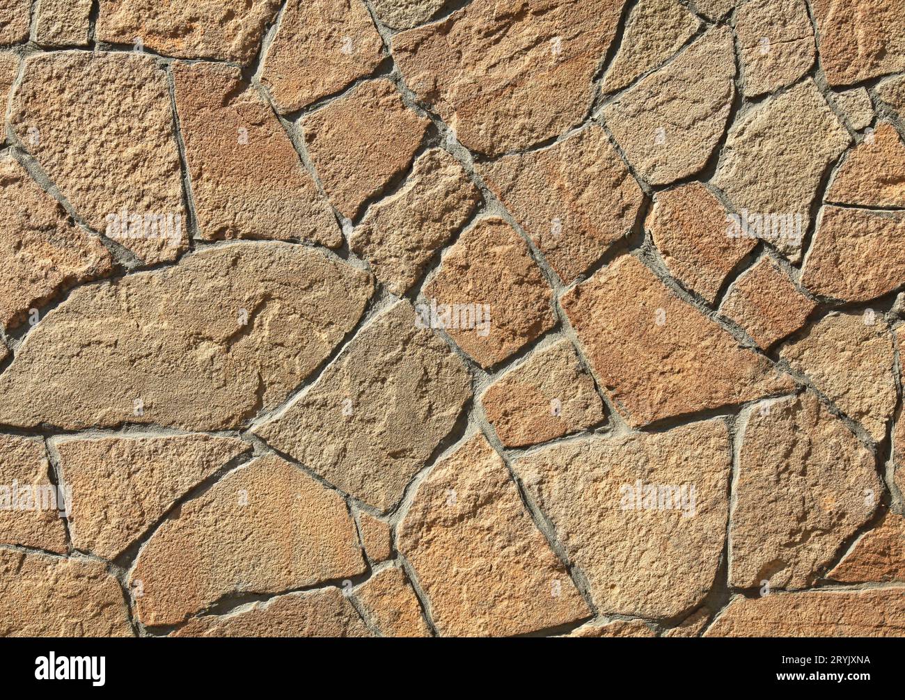 Granite stone wall, background. Mosaic structure of surface, made of granite rocks (bricks). The wall texture of volcanic yellow and brown color Stock Photo