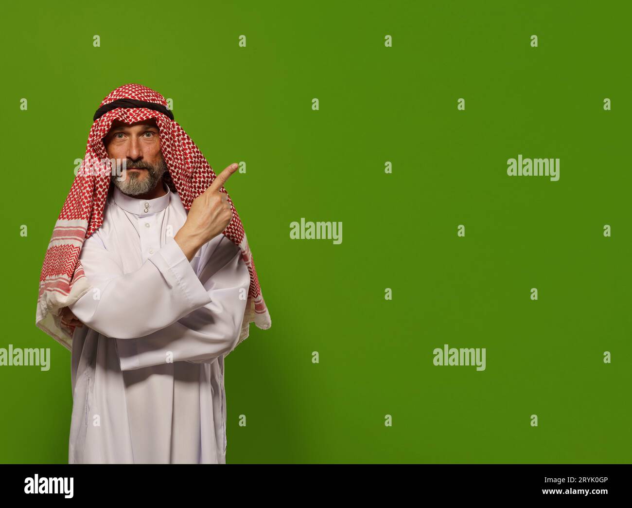 Mature Muslim man in a traditional dishdasha points his finger towards copy space symbolizing concept of Sharia law, the Islamic Stock Photo