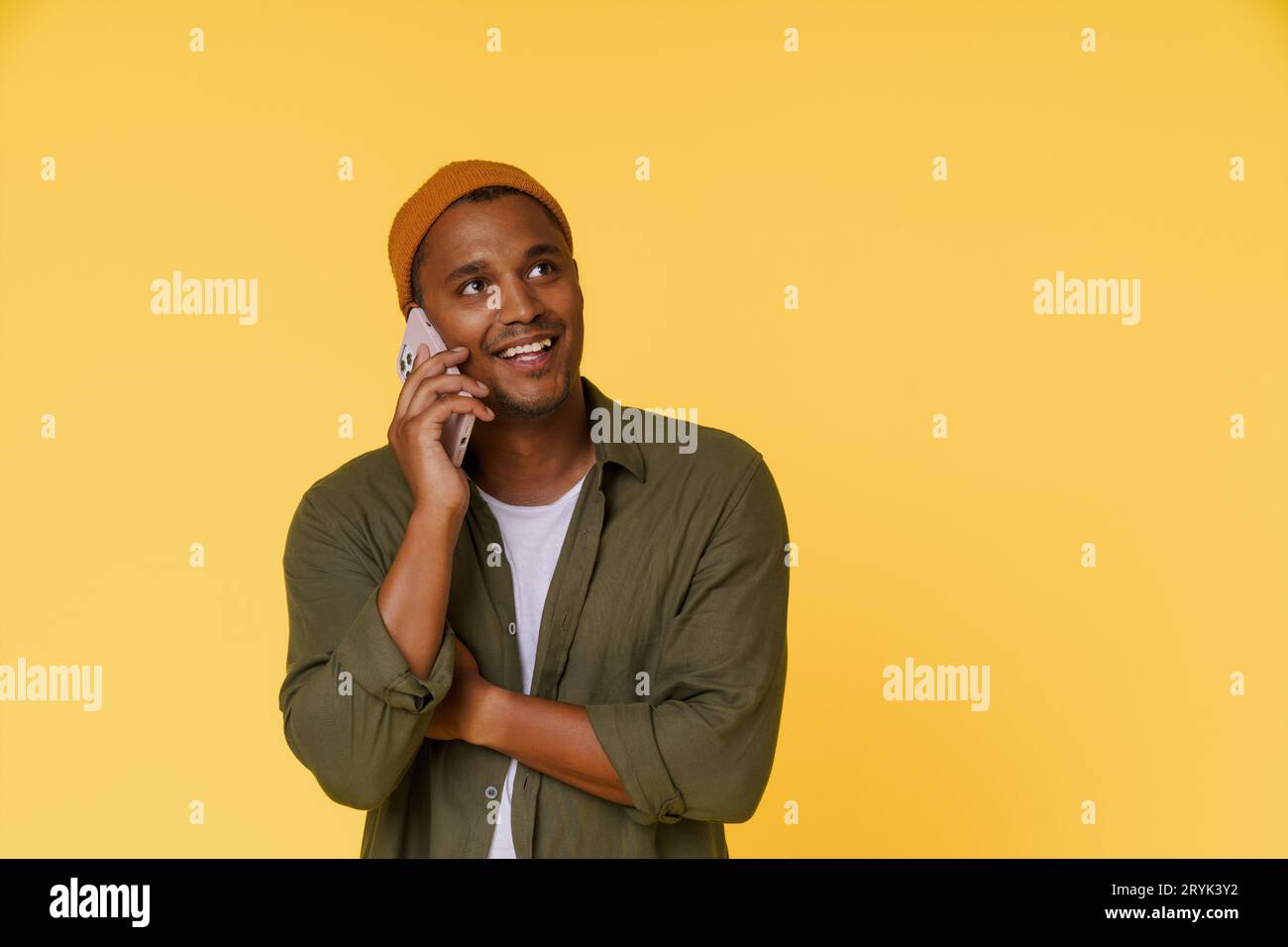 Smiling African man wearing orange cap is having phone call, with copy space on yellow background. Perfect for product placement Stock Photo