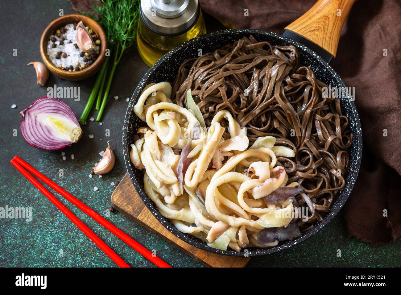 Spicy Noodles, Korean traditional food. Buckwheat soba noodles and squid with sour cream sauce on a dark stone table top. Stock Photo