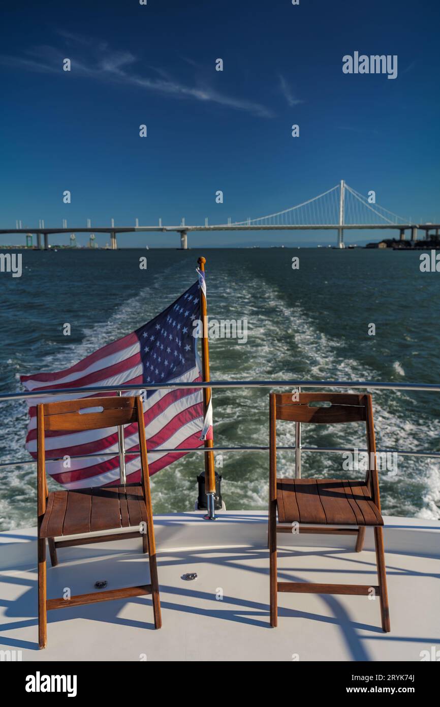Chairs on the deck of a yacht crossing San Francisco Bay with American Flag and Bay Bridge in background Stock Photo