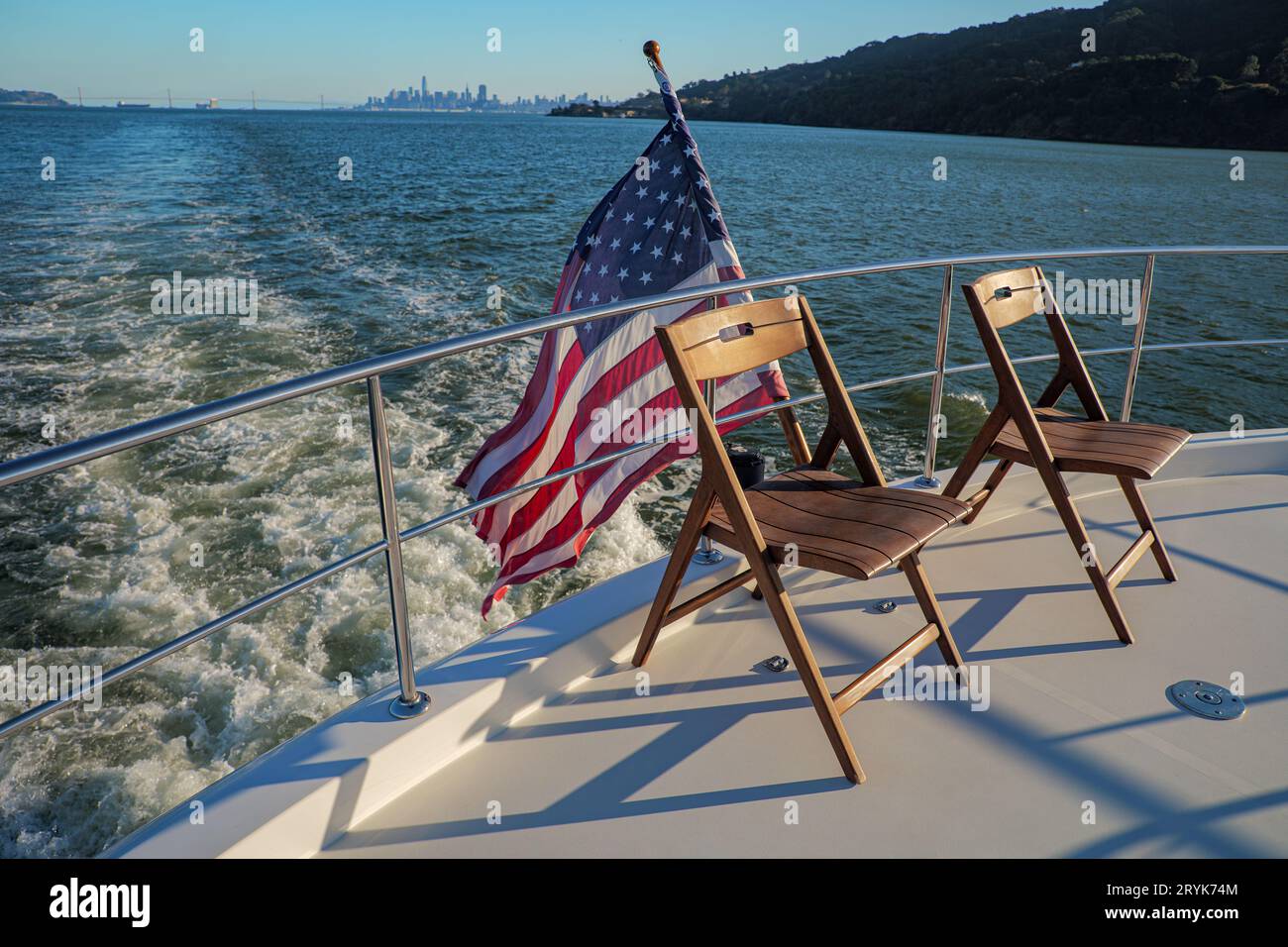 Chairs on the deck of a yacht crossing San Francisco Bay with American Flag and city in background Stock Photo