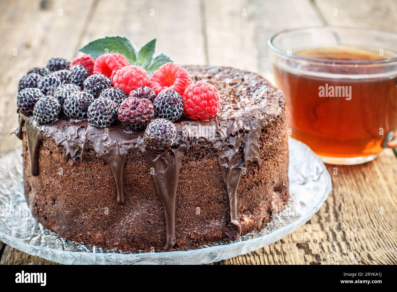 Homemade chocolate cake decorated with black and red raspberries on glass plate with cup of tea Stock Photo