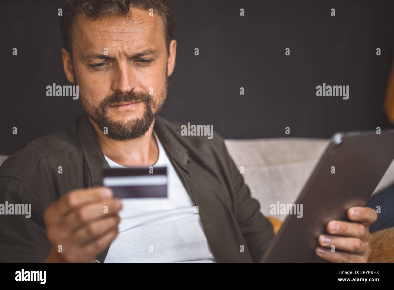 Man is seen sitting home and using his tablet PC for online shopping. He holding credit card in one hand and the tablet PC in th Stock Photo