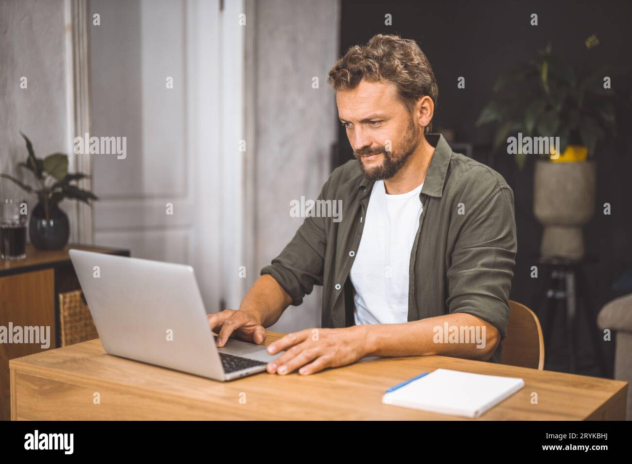 Modern freelancer lifestyle, man intently focused on laptop, sitting in cozy home office. Concept of working from home, emphasiz Stock Photo