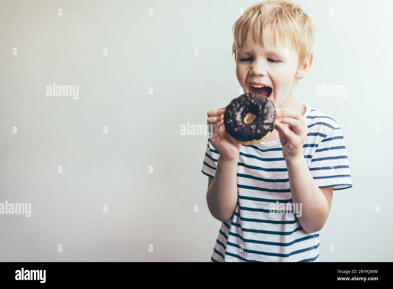 Teen boy bites a chocolate donut. Funny portrait of a child. Stock Photo