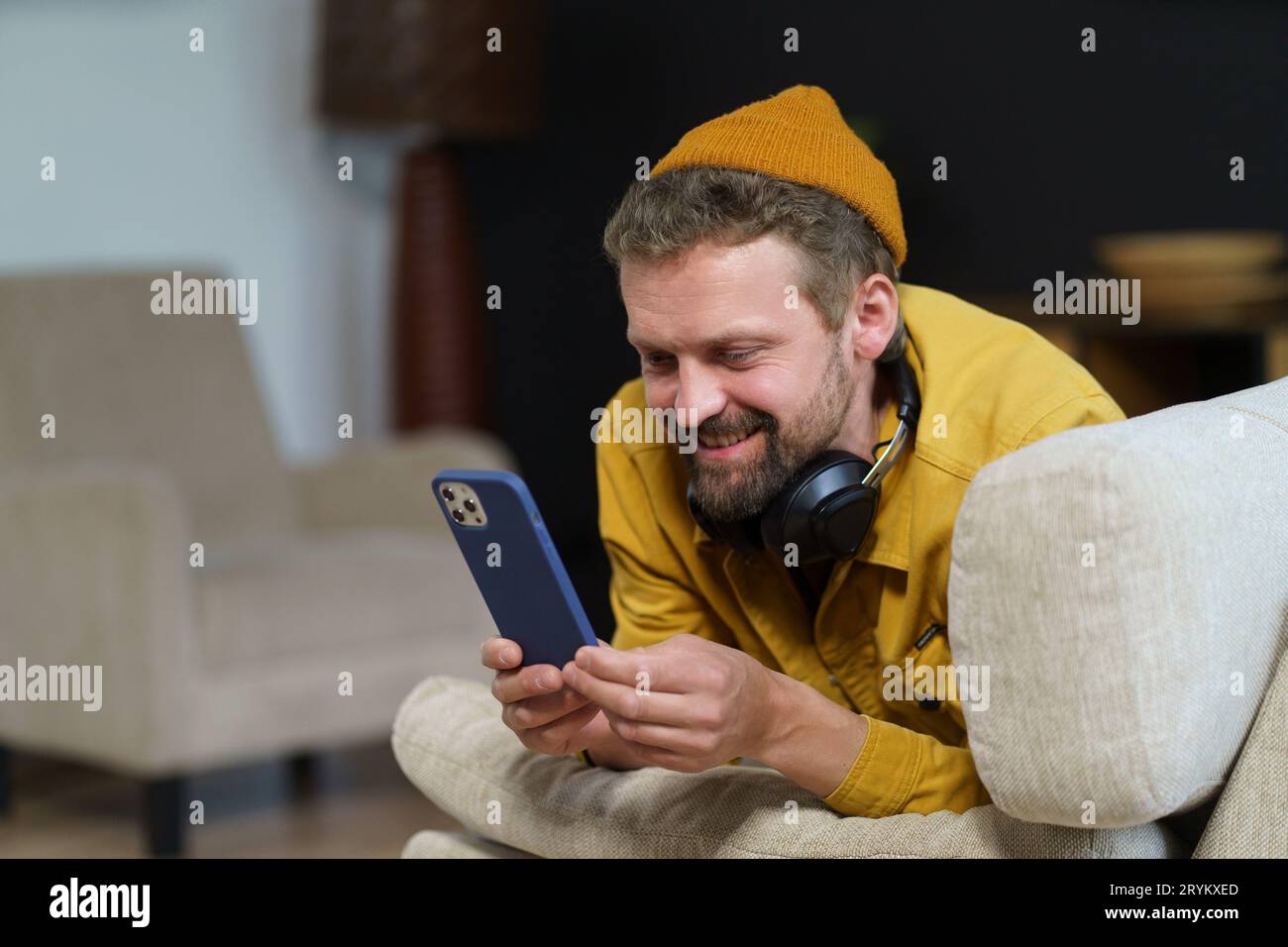Man in casual spending his leisure time home on sofa, engrossed in phone. He texting someone using messaging app, indicating act Stock Photo