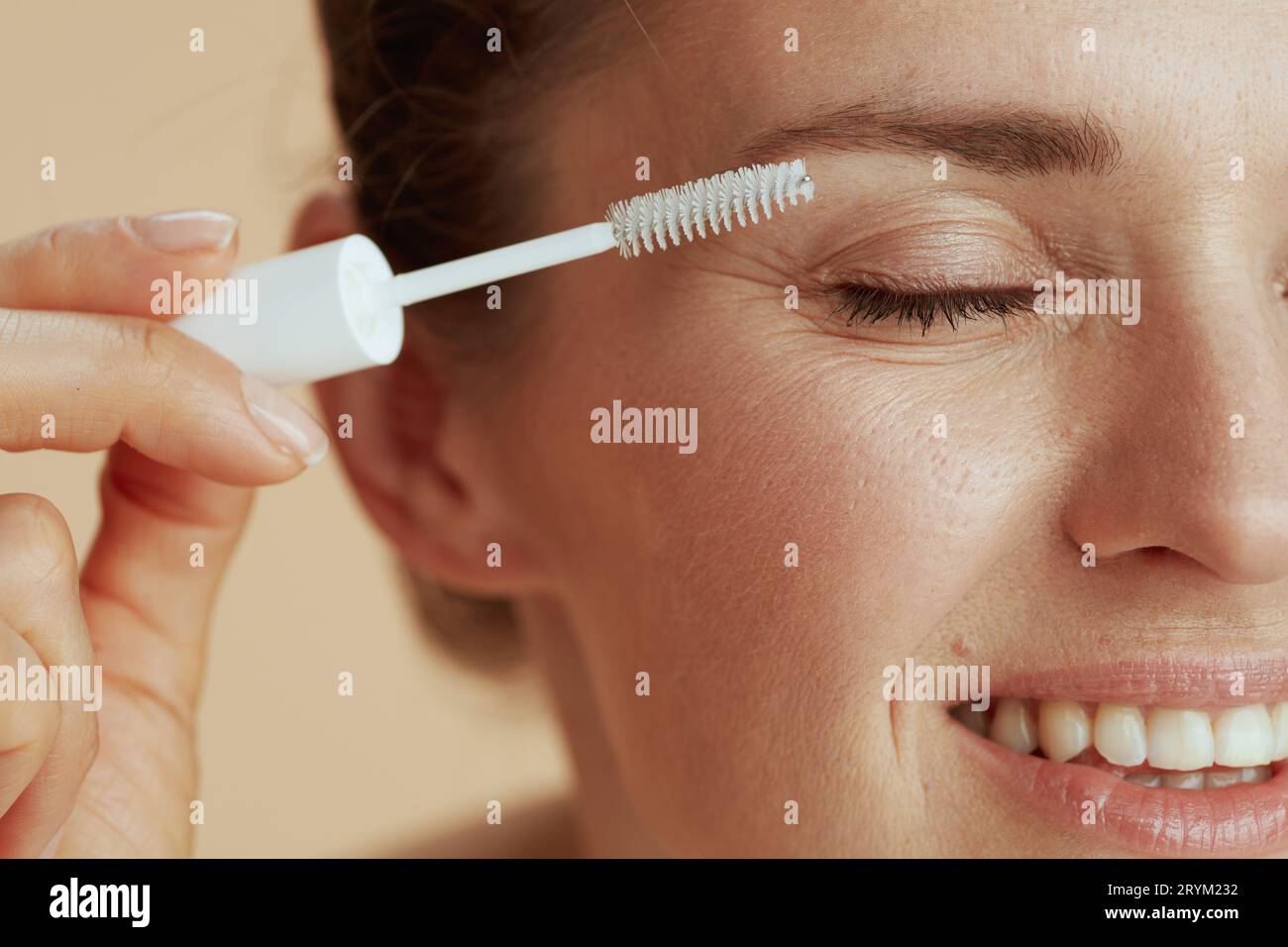 Closeup on modern 40 years old woman with brow brush isolated on beige background. Stock Photo