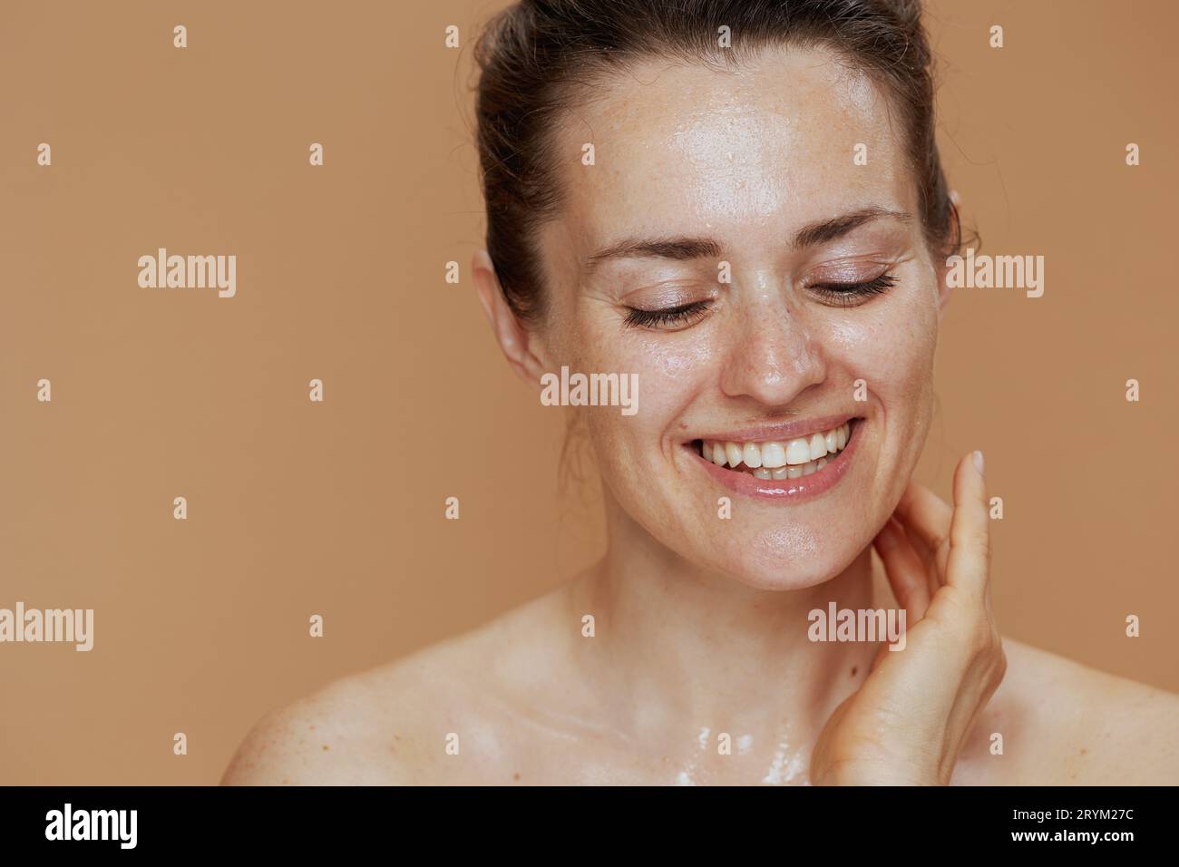 happy modern female with wet face washing against beige background