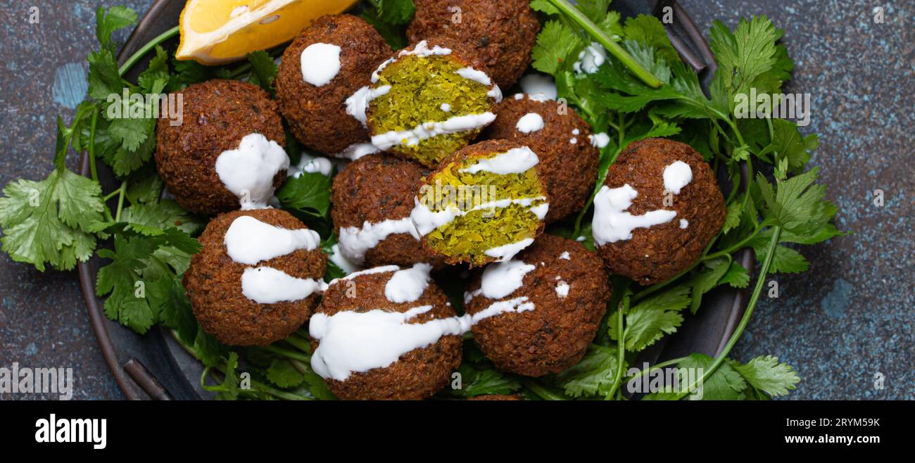 Plate of fried falafel balls served with fresh green cilantro and lemon, top view on rustic concrete background. Traditional veg Stock Photo