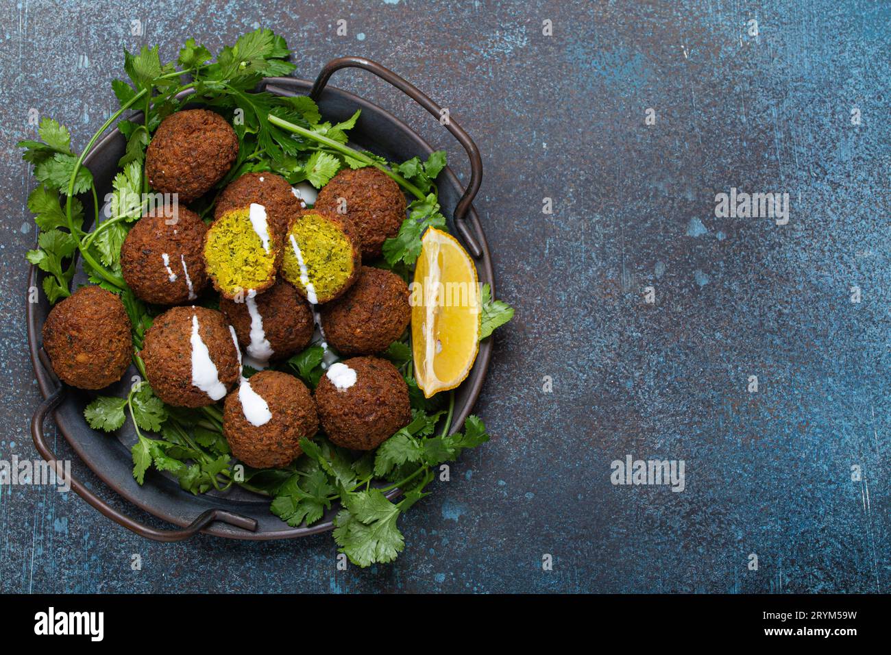 Plate of fried falafel balls served with fresh green cilantro and lemon top view on rustic concrete background. Traditional vega Stock Photo