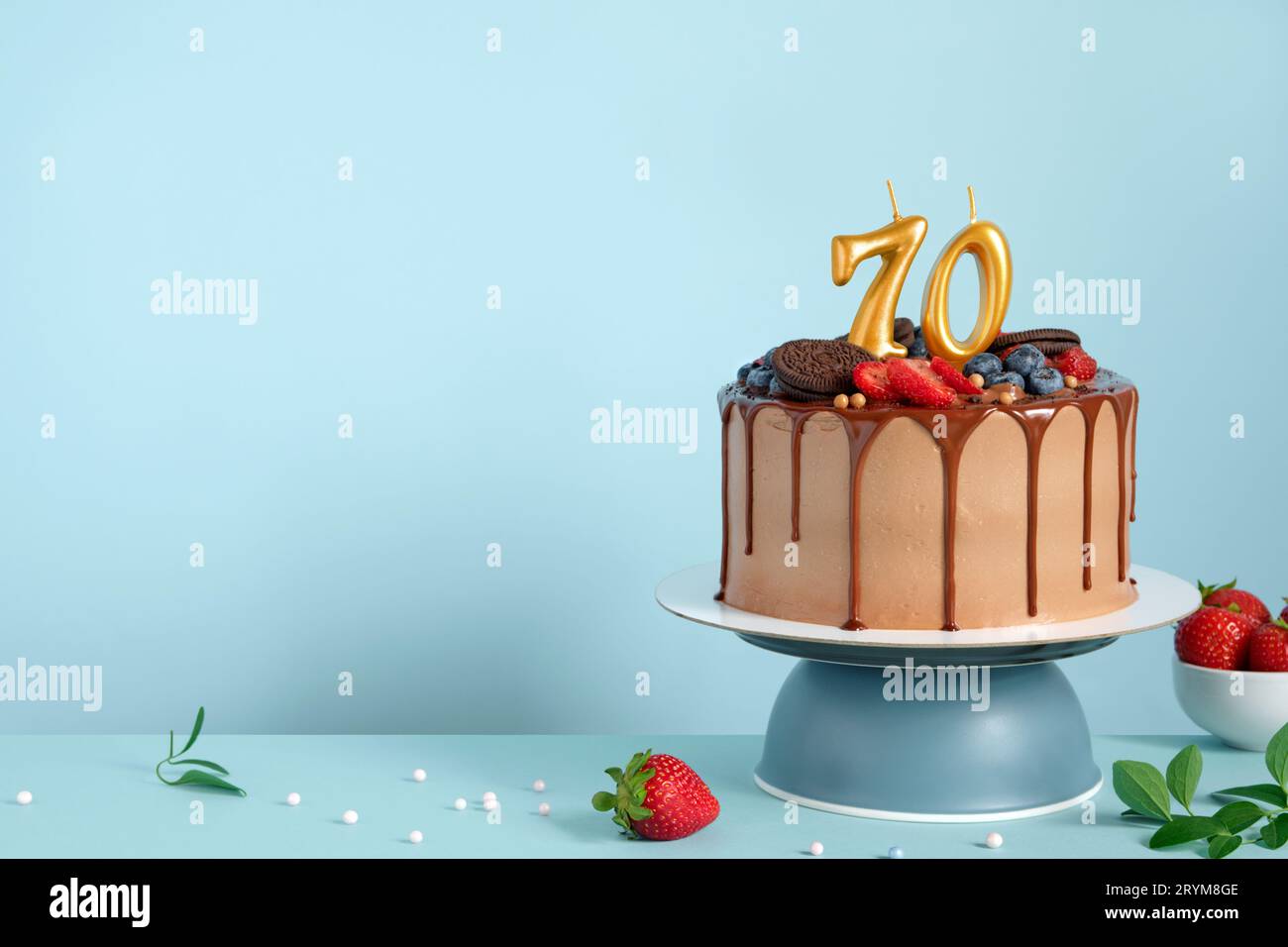Chocolate birthday cake with berries, cookies and number seventy golden candles on blue wall background, copy space Stock Photo
