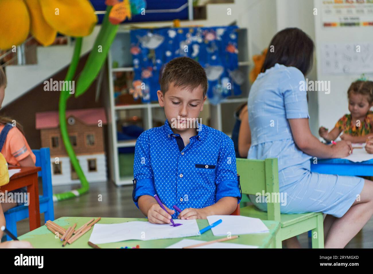 Creative kids during an art class in a daycare center or elementary school classroom drawing with female teacher. Stock Photo