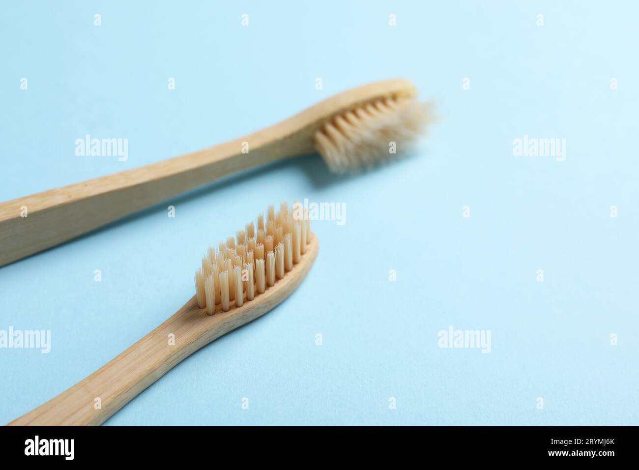 Two bamboo toothbrushes on light blue background, closeup. Space for ...