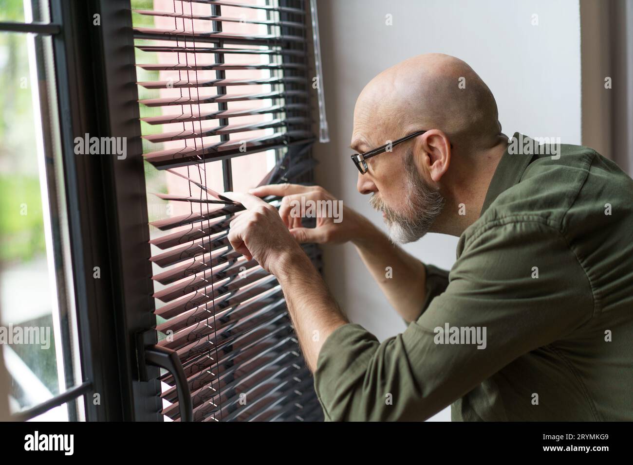 Concept of neighbors through perspective of old man standing near window and watching outside world. Senior's curiosity and enga Stock Photo