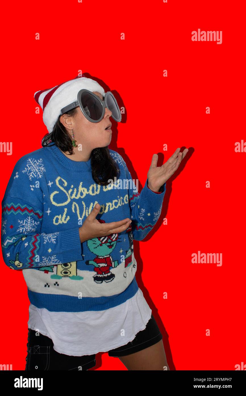 Woman with long hair, making a surprised gesture looking upwards where there is blank space for text. The woman is wearing a blue ugly sweater, a Chri Stock Photo