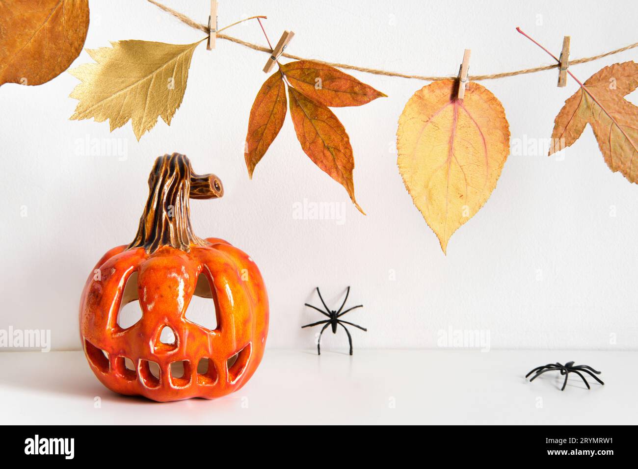 Ceramic pumpkin jack lantern and autumn leaves garland on table wall background. Home decoration Stock Photo