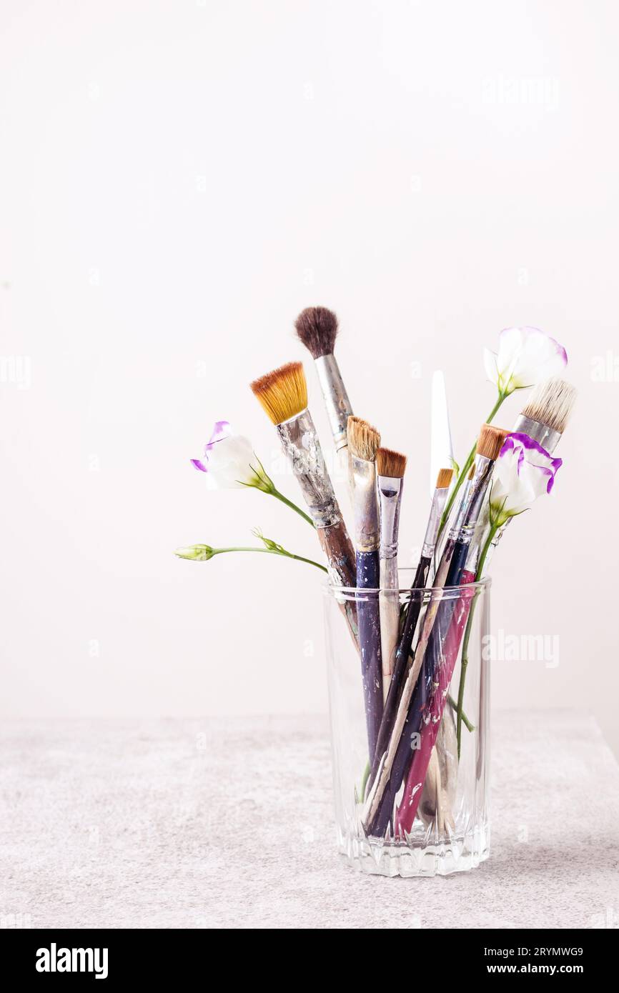 Glass with artistic brushes and flowers on gray table Stock Photo