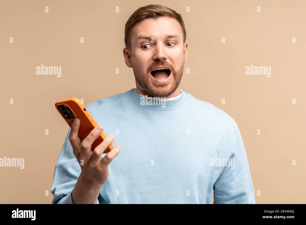 Shocked screaming confused man looking at smartphone screen on beige ...