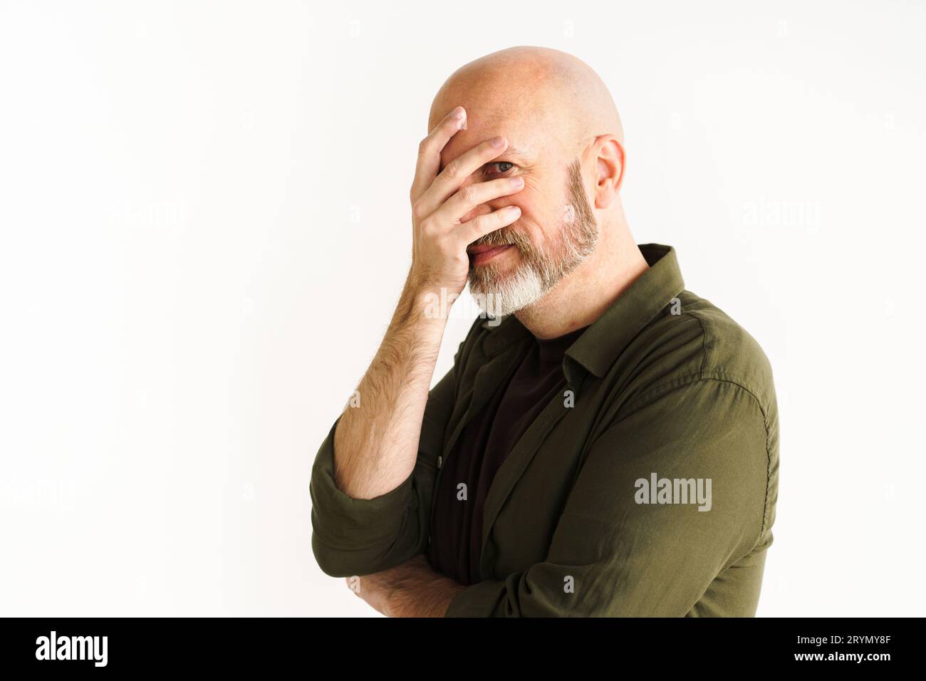 Mature man with silver beard in moment of frustration or disbelief. He puts hand on face in facepalm gesture, conveying sense of Stock Photo