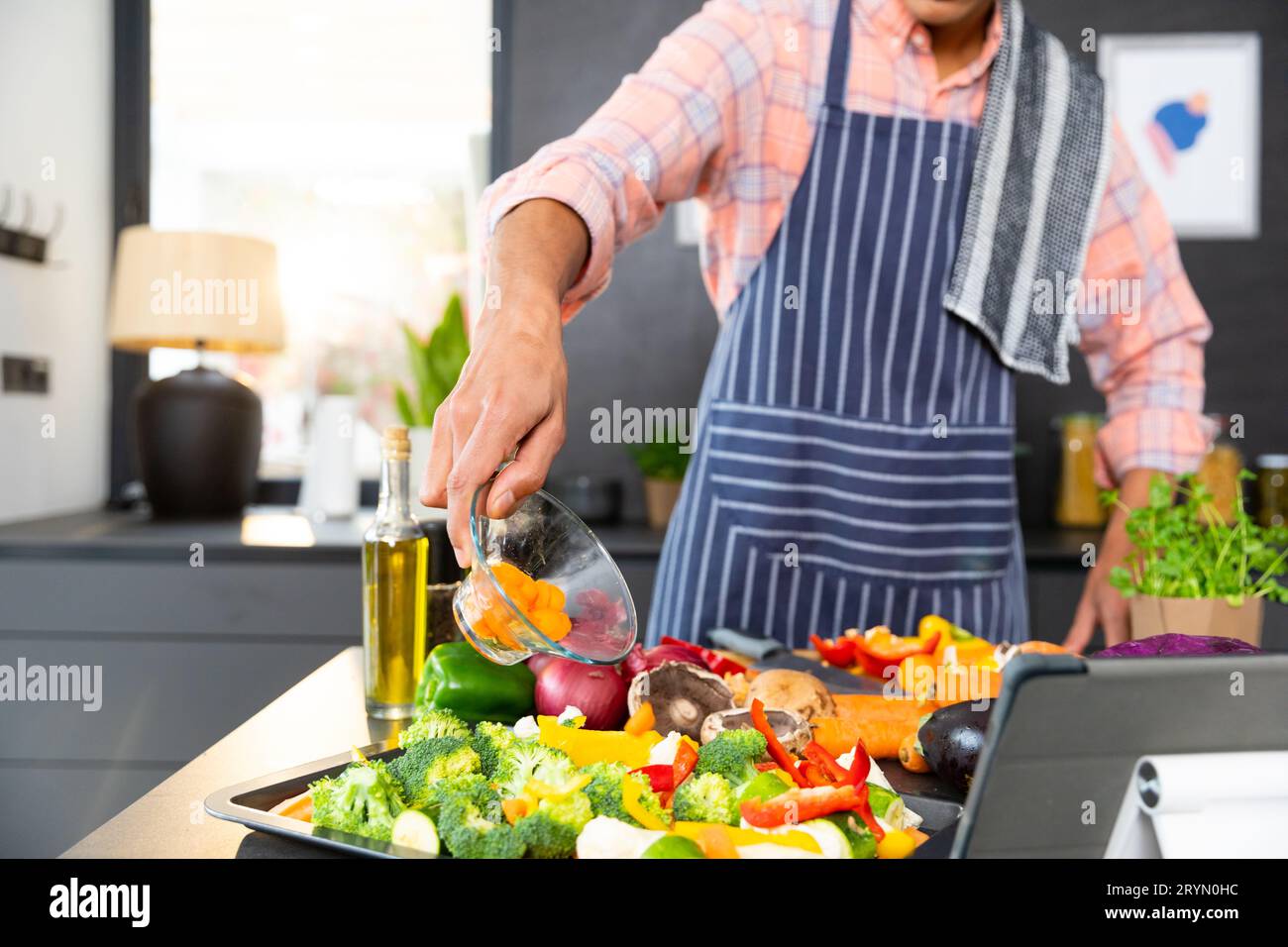 https://c8.alamy.com/comp/2RYN0HC/midsection-of-biracial-man-wearing-apron-cooking-dinner-pouring-vegetables-in-kitchen-2RYN0HC.jpg