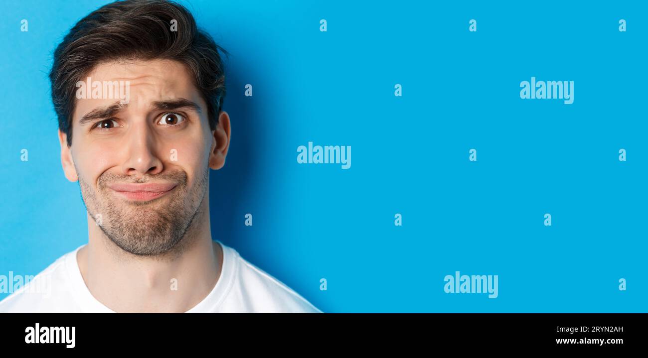 Head shot of skeptical and disappointed man, grimacing complicated, standing against blue background Stock Photo